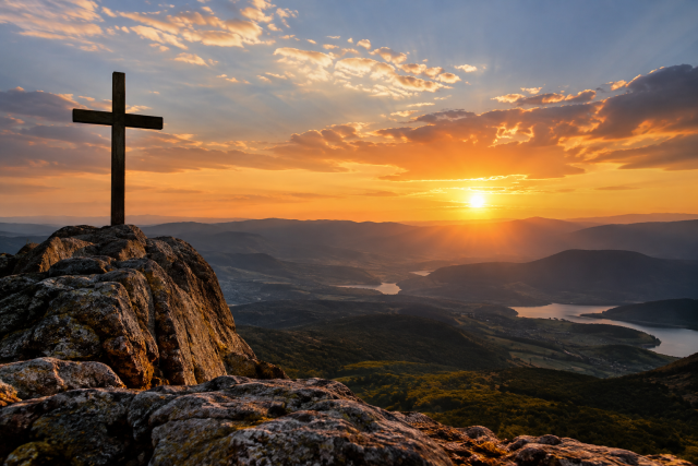 Cruz no alto de uma montanha diante do pôr do sol